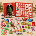 A Christmas advent calendar set with a red open box showing numbered doors and Santa illustrations, surrounded by assorted festive toys and small gifts on a beige surface with blurred evergreen branches and lights in the background.