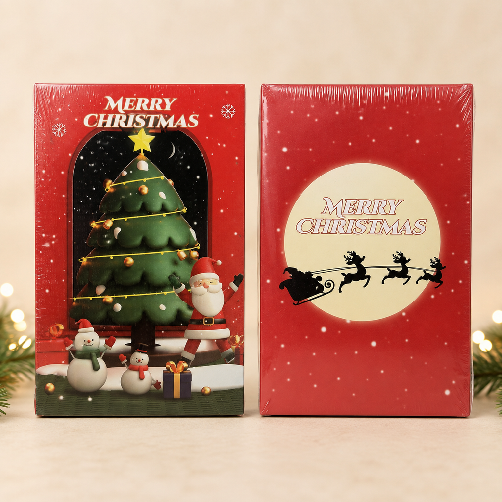 Two Christmas-themed gift boxes standing side by side on a light beige surface. The left box shows a festive Christmas tree scene with Santa, snowmen, and the words “MERRY CHRISTMAS.